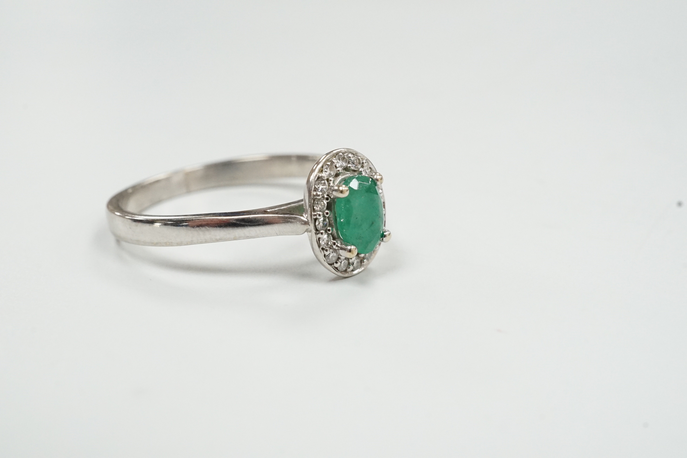A modern 18ct white gold, emerald and diamond set oval cluster ring, size S, gross weight 3 grams.